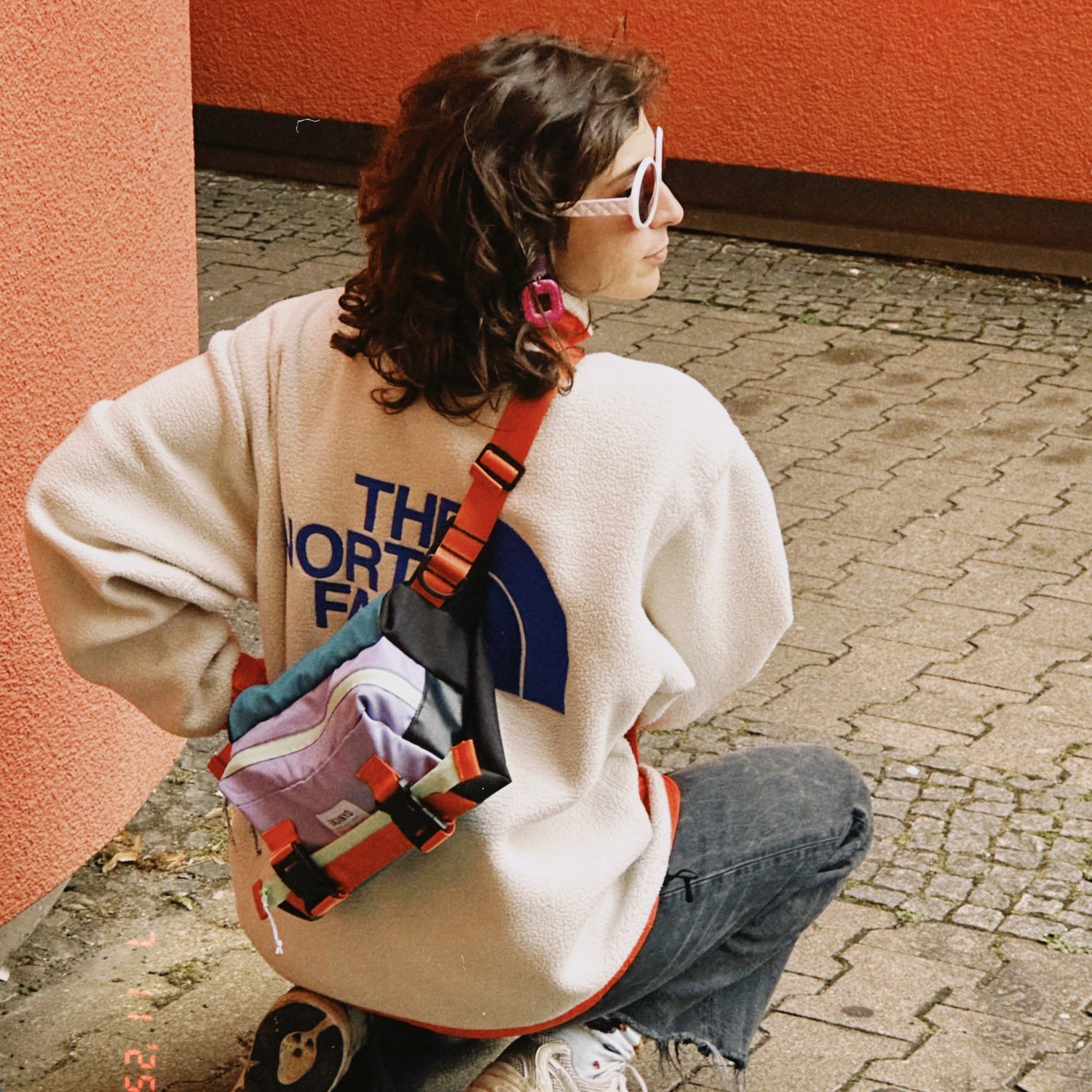 Person wearing a white sweatshirt with a brand logo, sitting on a cobblestone street.